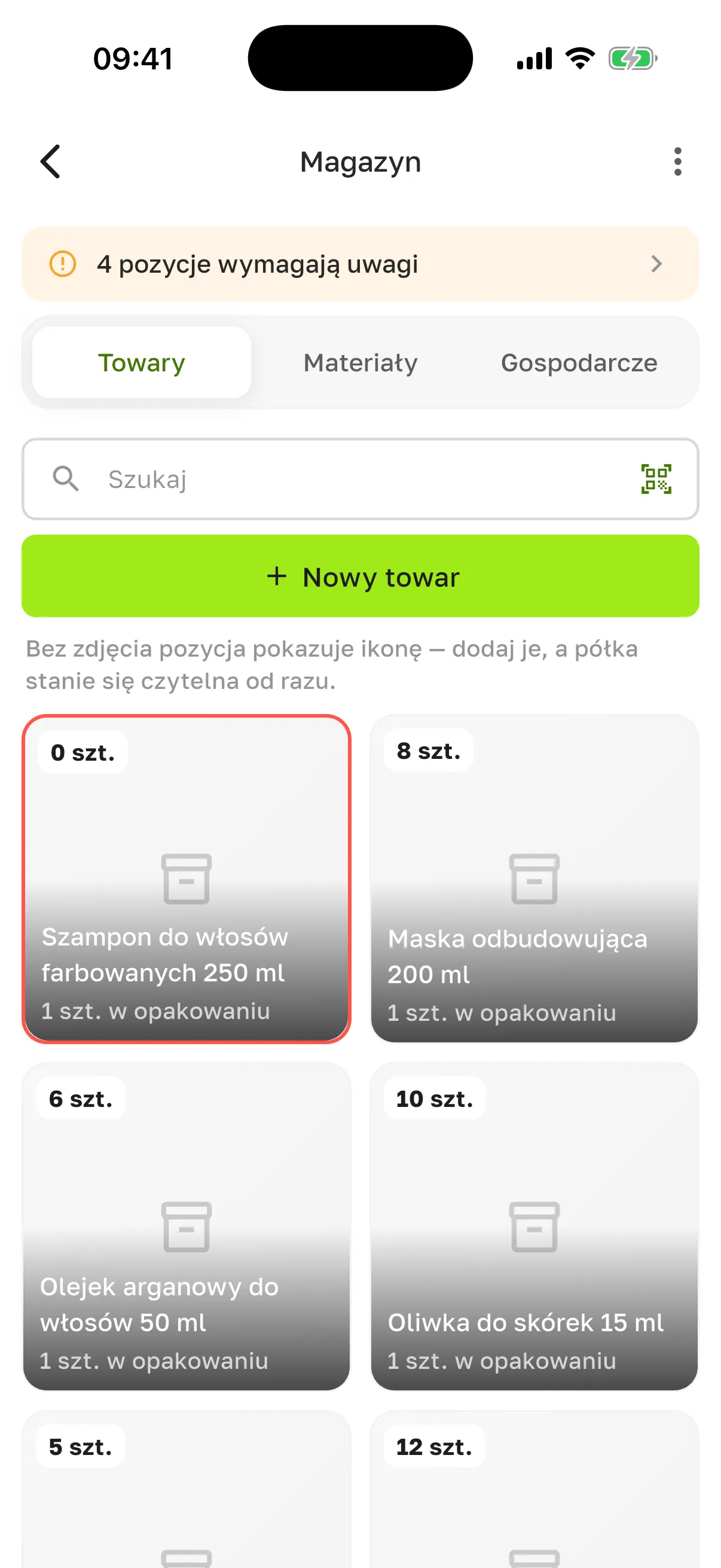 Ekran „Magazyn”: pasek „4 pozycje wymagają uwagi”, zakładki „Towary”, „Materiały”, „Gospodarcze”, pole „Szukaj” z ikoną skanowania, przycisk „Nowy towar” i kafelki towarów ze stanem: „Szampon do włosów farbowanych 250 ml” 0 szt. w czerwonej ramce, „Maska odbudowująca 200 ml” 8 szt., „Olejek arganowy do włosów 50 ml” 6 szt., „Oliwka do skórek 15 ml” 10 szt.